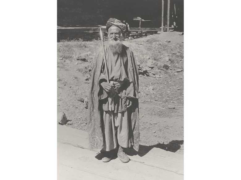 Der um 1896 vor der Islamisierung durch Abdur Rahman Khan aus Afghanistan geflüchtete Kati-Kafire Bagash mit Zeremonialaxt und besticktem Mantel. Zusätzlich zum Ledergürtel trägt er einen geschlungenen Stoffgürtel und anstelle der traditionellen Kappe einen 'islamischen' Turban.