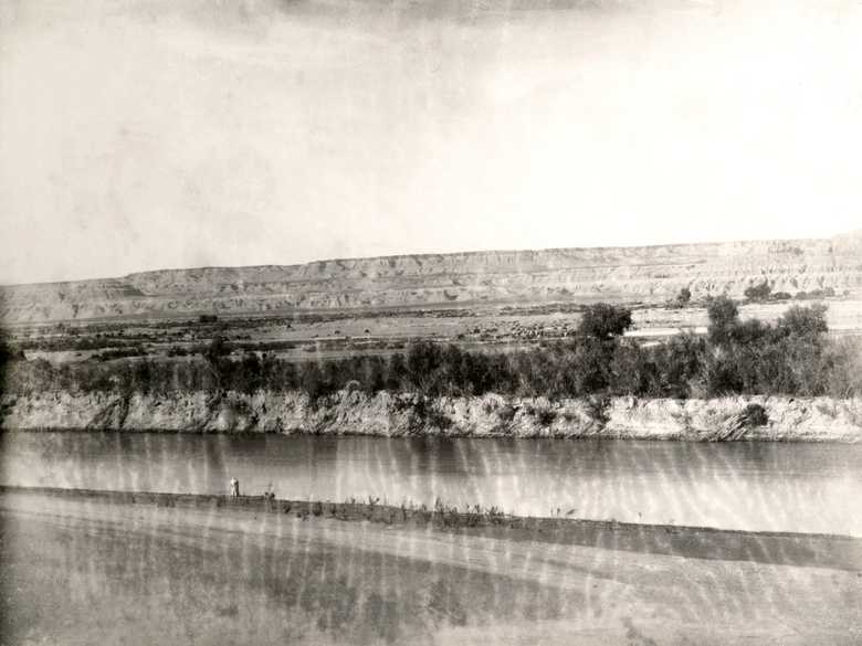 General view from the southern bank of the meandering Hilmand River, north of Rudbar, to its terraced steep cliff in the background. Some horses and camels are grazing on the opposite bank of the river.
